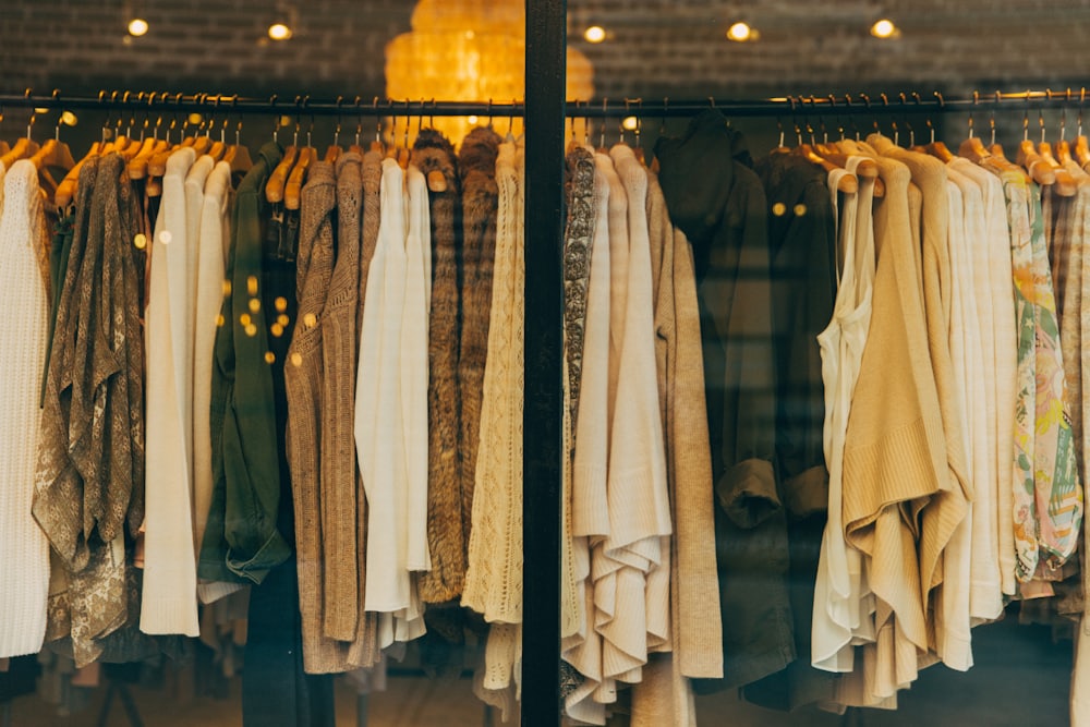A shop window filled with a rail of cream and neutral knitwear, lit from inside.